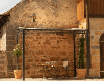 Pergola Elba in pulverbeschichtet anthrazit mit Sonnensegel an einer Sandsteinwand angelehnt