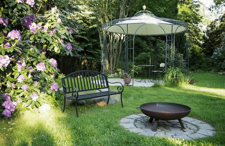 Pavillon Florenz mit Zubehör in einem begrünten Garten mit Feuerschale
